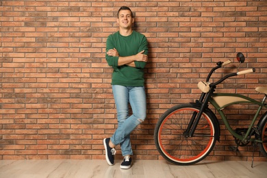 Photo of Portrait of handsome young man with bicycle near brick wall