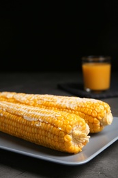 Photo of Delicious boiled corn cobs with butter on gray table against black background. Space for text