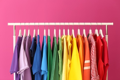 Rack with rainbow clothes on color background