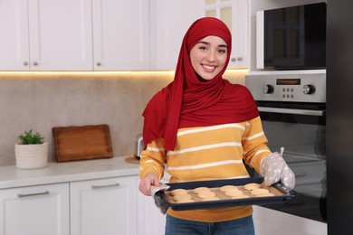 Muslim woman holding tray with cookies in kitchen. Space for text