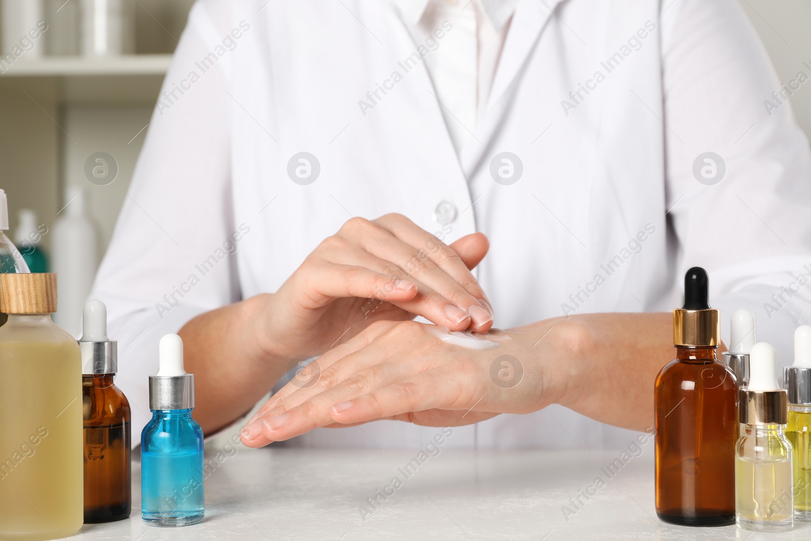 Photo of Dermatologist testing cosmetic product at white table indoors, closeup