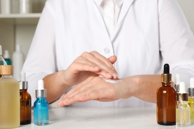 Photo of Dermatologist testing cosmetic product at white table indoors, closeup