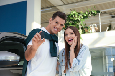 Photo of Happy couple with car key in modern auto dealership