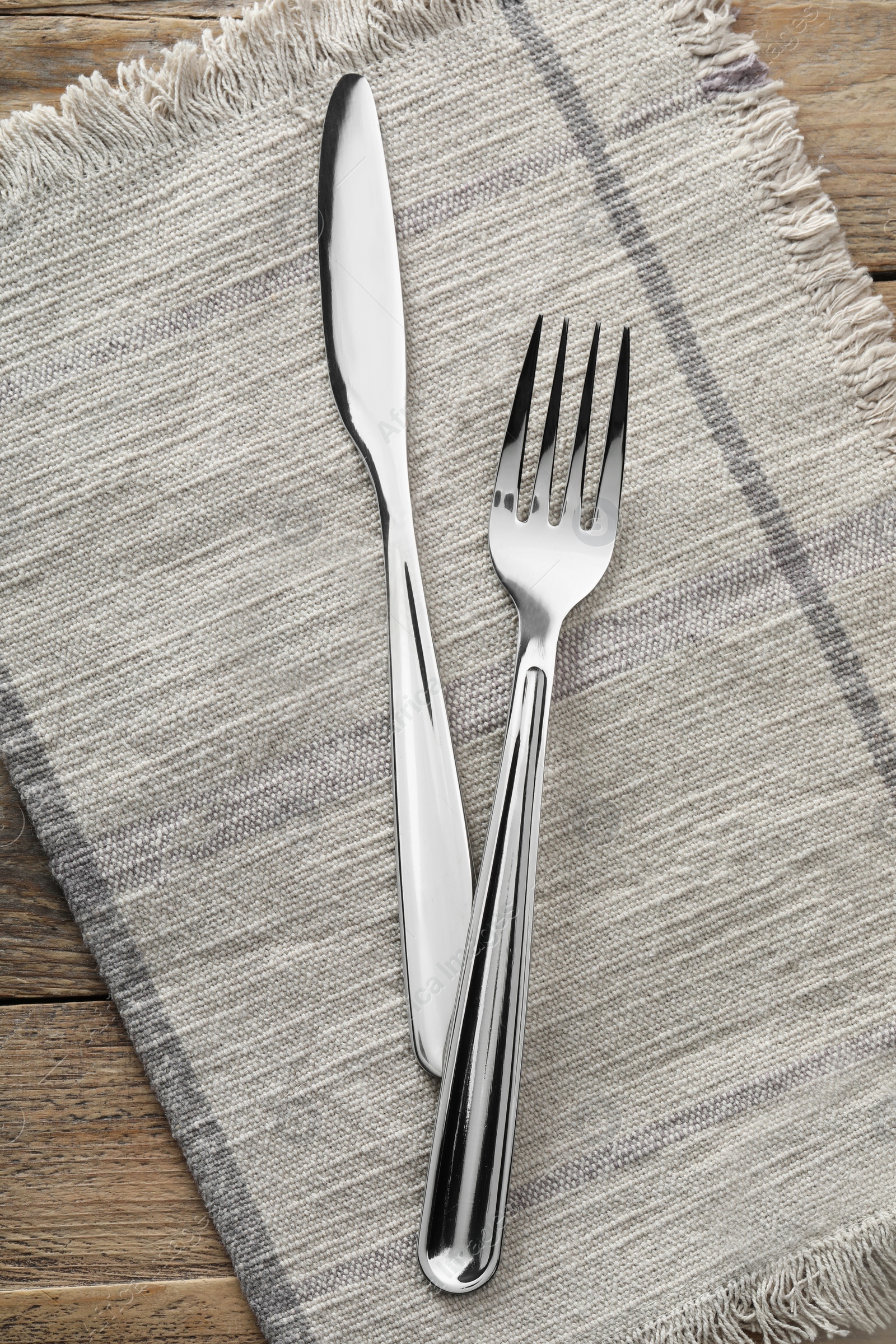 Photo of Fork, knife and napkin on wooden table, top view. Stylish shiny cutlery set