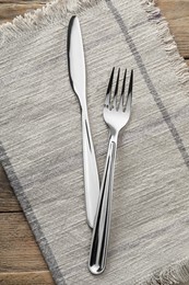 Photo of Fork, knife and napkin on wooden table, top view. Stylish shiny cutlery set