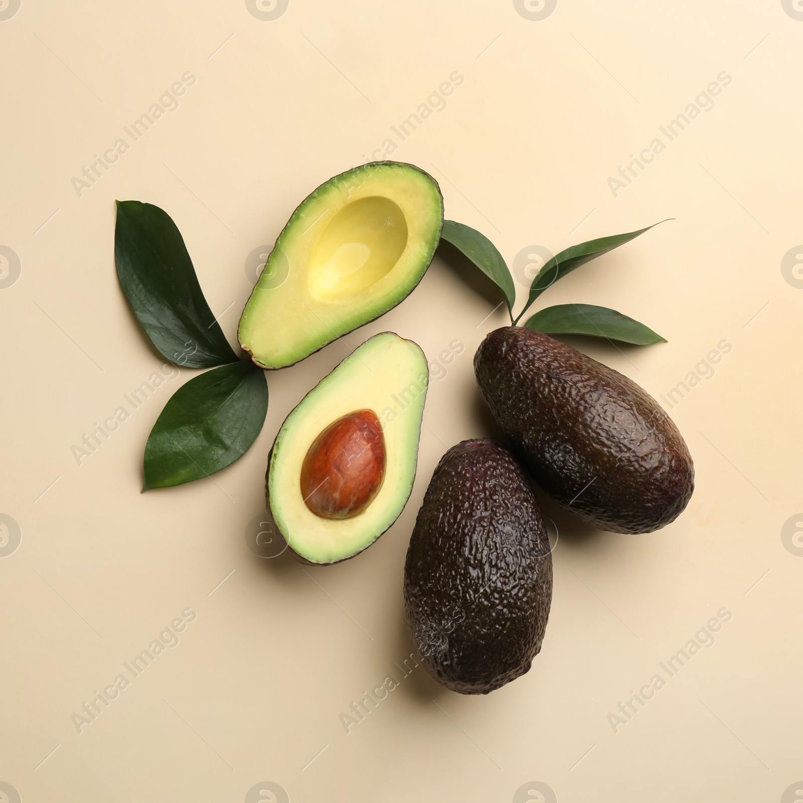 Photo of Whole and cut ripe avocadoes with green leaves on beige background, flat lay