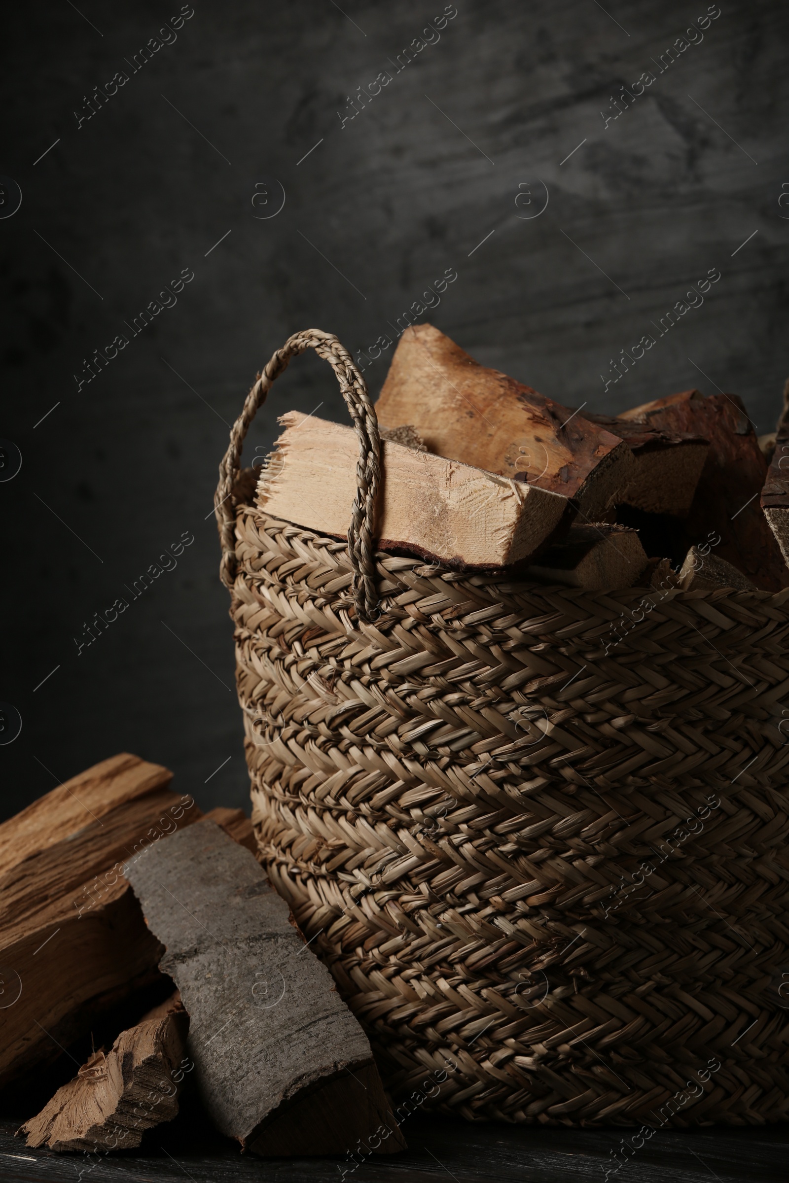 Photo of Wicker basket with cut firewood on black table