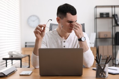 Photo of Young man with glasses suffering from headache at workplace in office