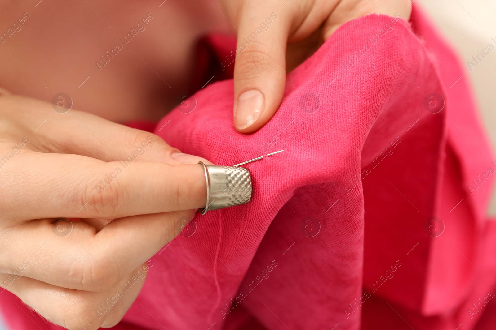 Photo of Woman sewing on red fabric with thimble and needle, closeup