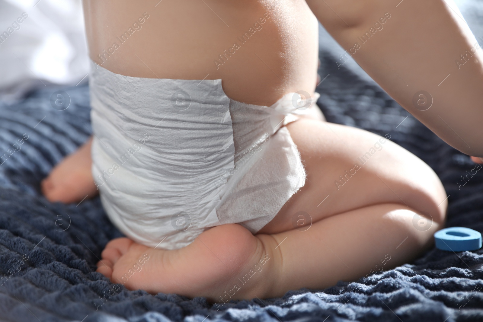 Photo of Cute little baby in diaper on bed at home, closeup