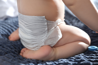 Cute little baby in diaper on bed at home, closeup