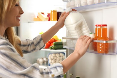 Photo of Young woman taking gallon of milk from refrigerator indoors