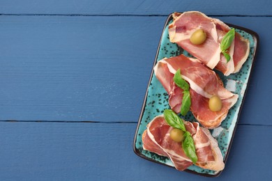 Photo of Tasty sandwiches with cured ham and basil on blue wooden table, top view. Space for text