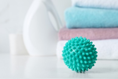 Turquoise dryer ball on white table, closeup. Space for text