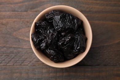 Photo of Sweet dried prunes in bowl on wooden table, top view