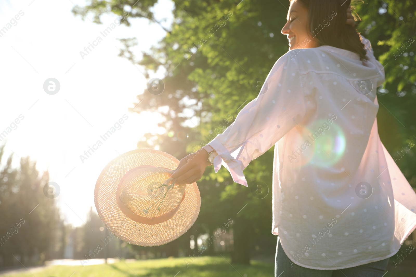Photo of Young woman with straw hat and flowers outdoors on sunny day, back view