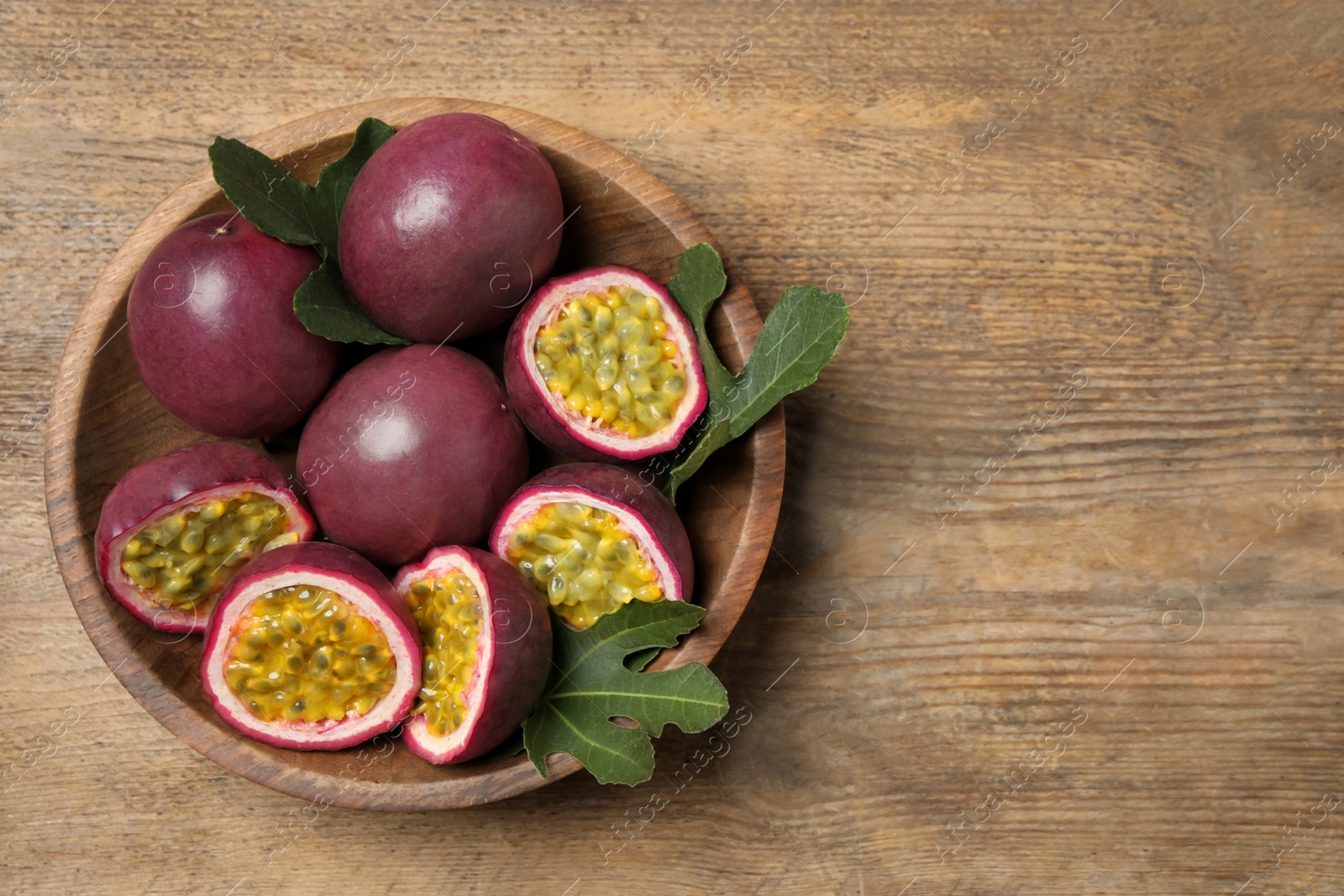 Photo of Cut and whole passion fruits (maracuyas) on wooden table, top view. Space for text