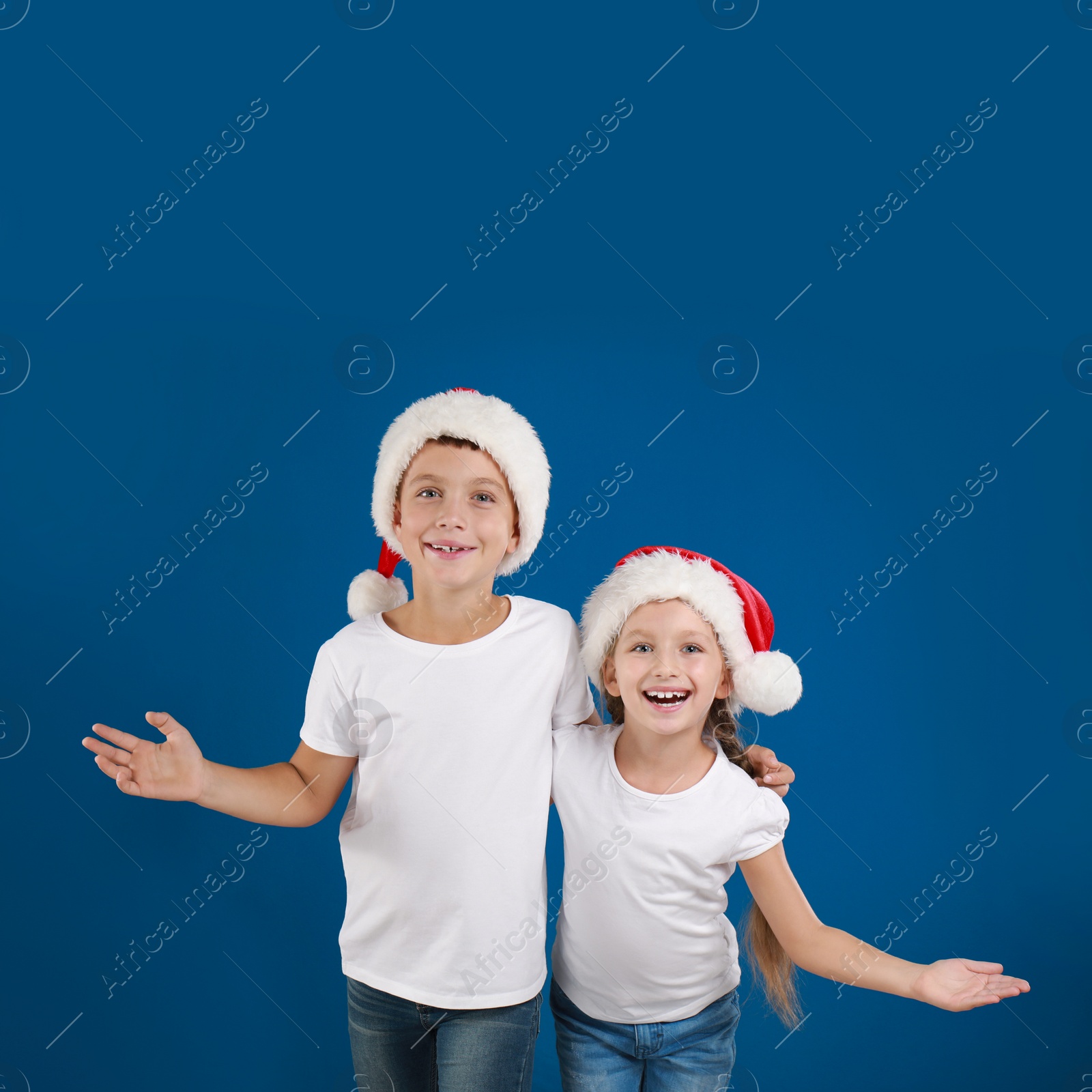 Image of Happy little children in Santa hats on blue background. Christmas celebration