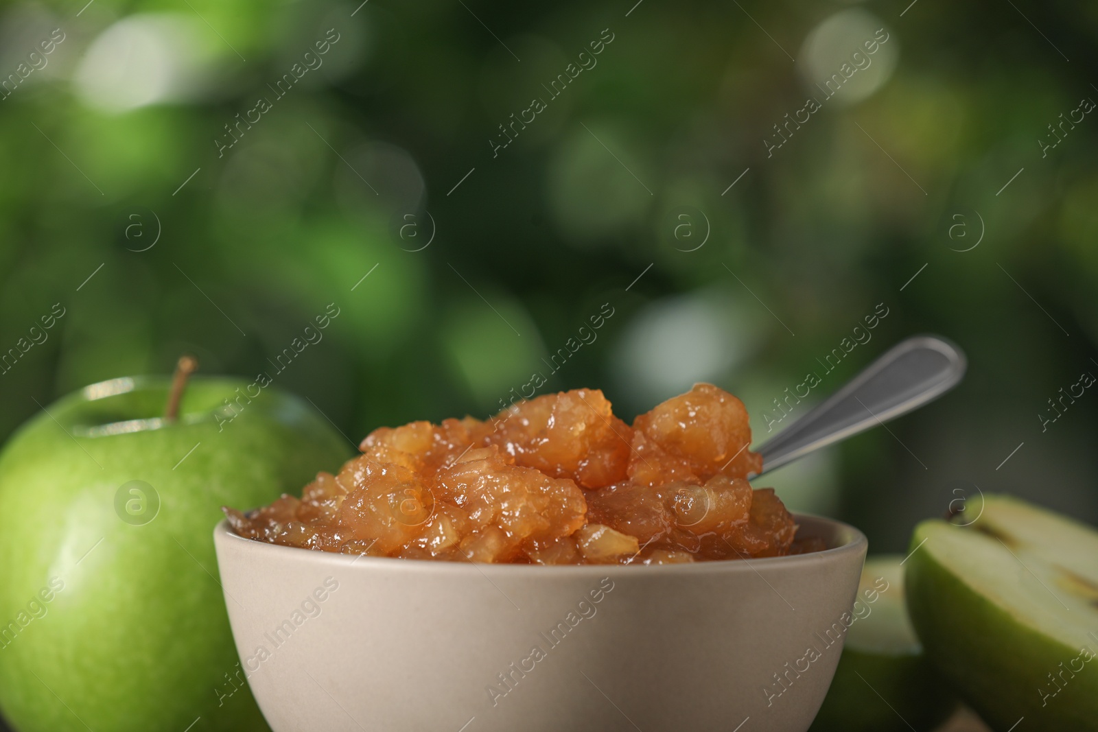 Photo of Bowl with delicious apple jam and fresh fruits against blurred background, closeup. Space for text