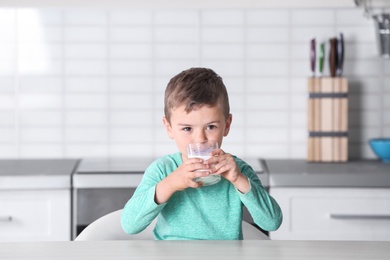 Cute little boy drinking milk at table in kitchen