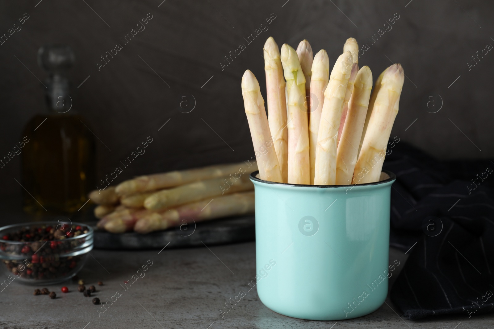 Photo of Fresh white asparagus in mug on grey table. Space for text