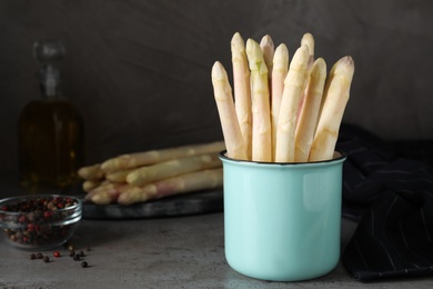 Photo of Fresh white asparagus in mug on grey table. Space for text