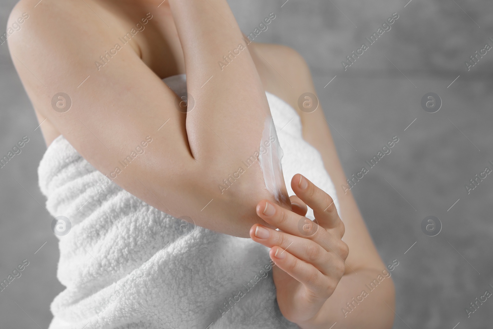 Photo of Woman applying body cream onto elbow on grey background, closeup. Space for text