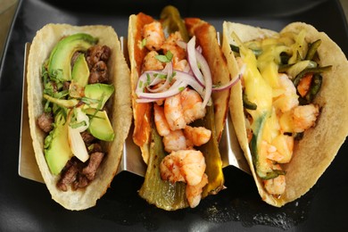 Photo of Delicious tacos with shrimps and vegetables on black plate