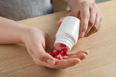 Photo of Woman pouring pills from bottle at wooden table, closeup