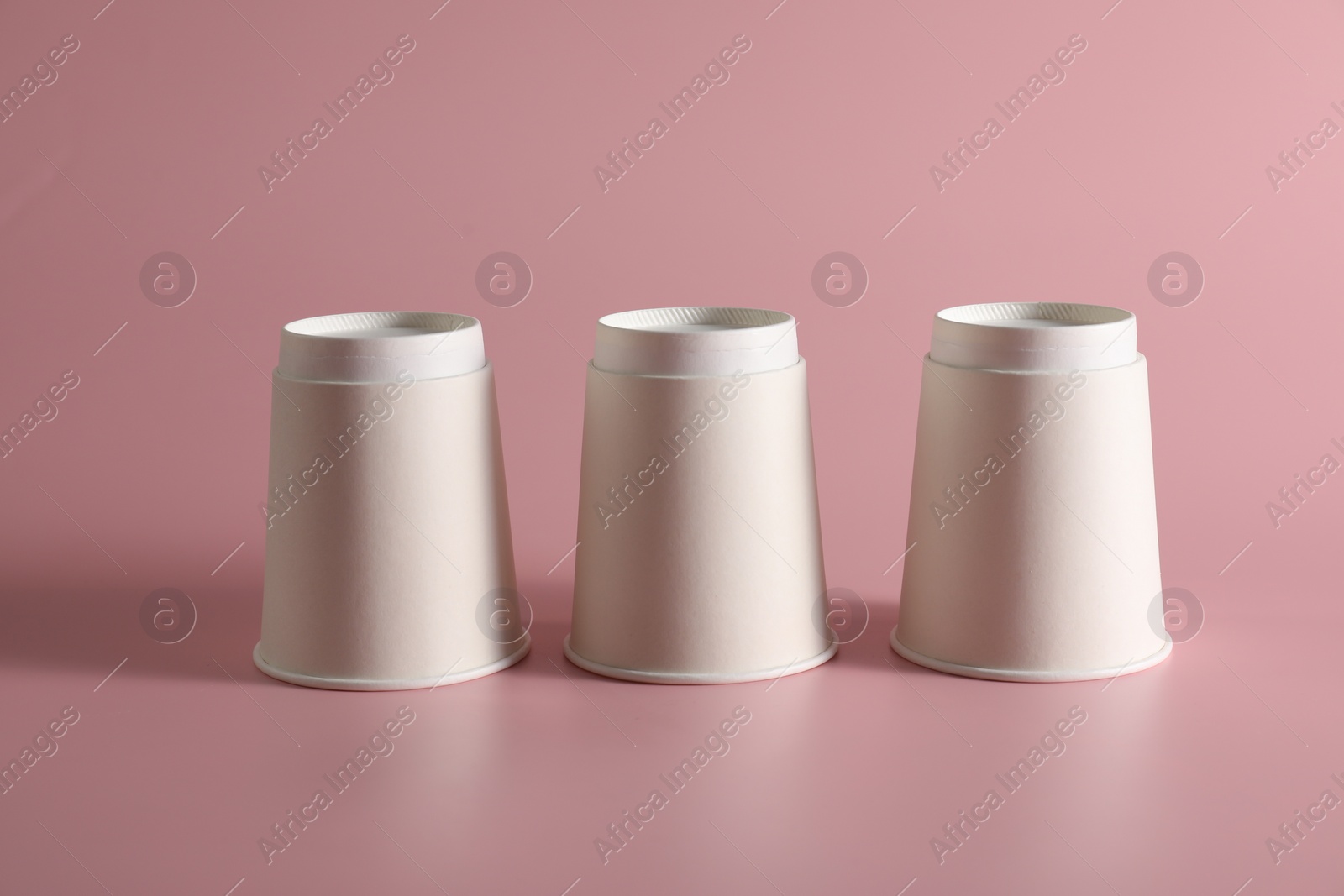 Photo of Shell game. Three paper cups on pink background