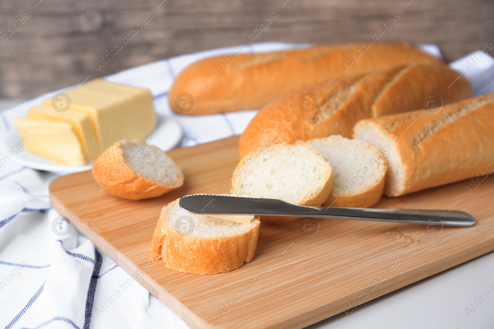 Photo of Tasty cut baguette with fresh butter on white table