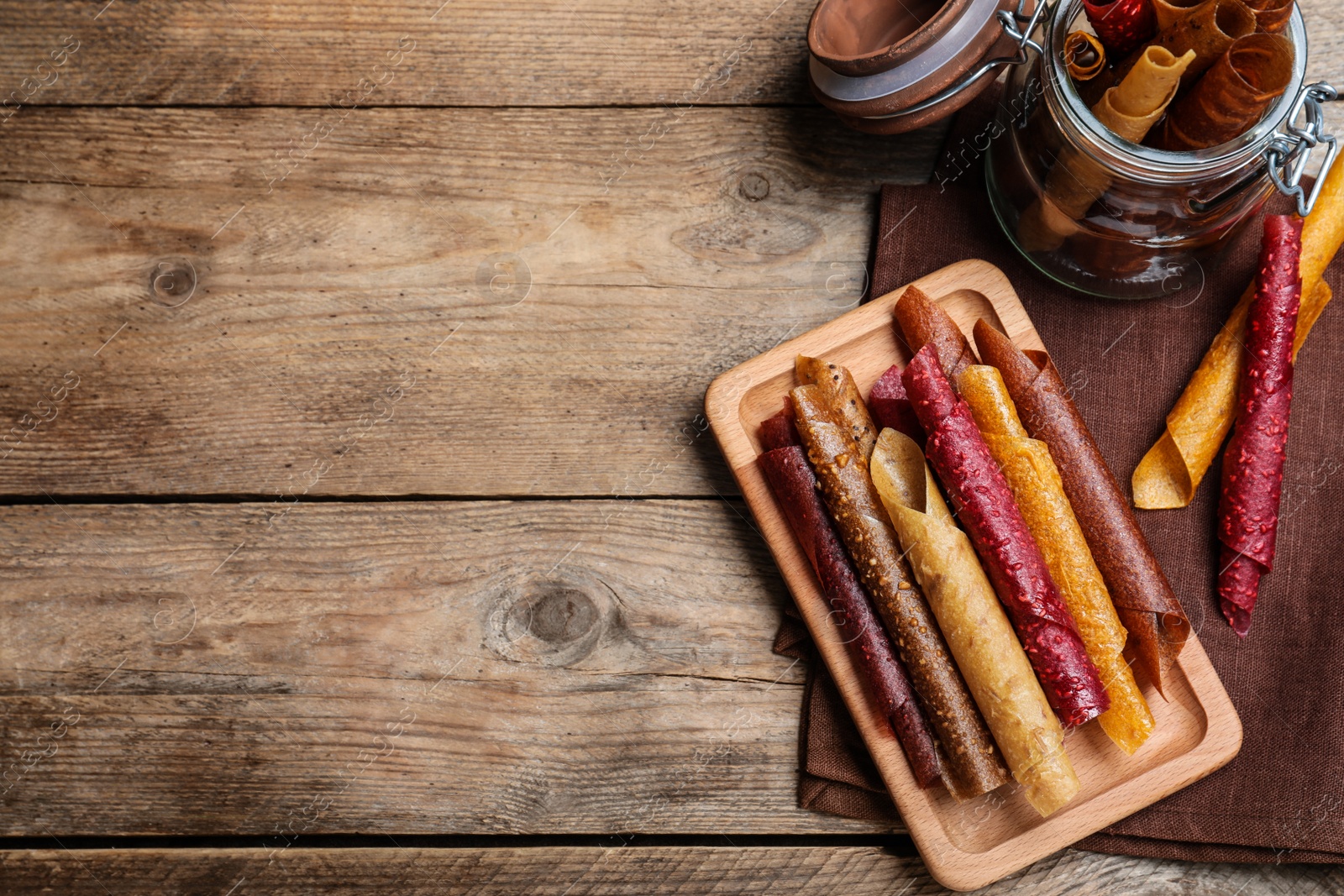 Photo of Delicious fruit leather rolls on wooden table, flat lay. Space for text