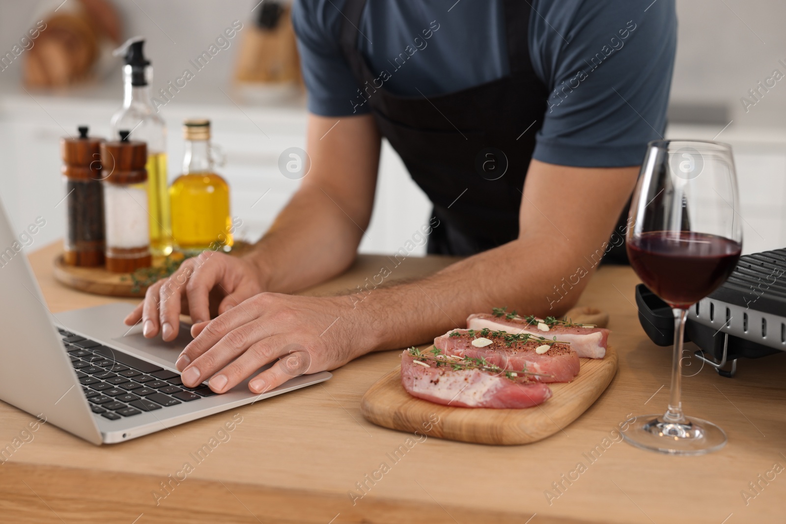 Photo of Man making dinner while watching online cooking course via laptop in kitchen, closeup