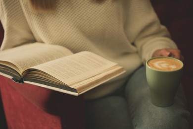 Image of Woman with cup of coffee reading book indoors, closeup