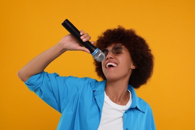 Photo of Curly young woman in sunglasses with microphone singing on yellow background