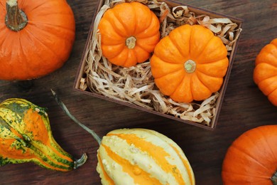 Photo of Crate and many different pumpkins on wooden table, flat lay