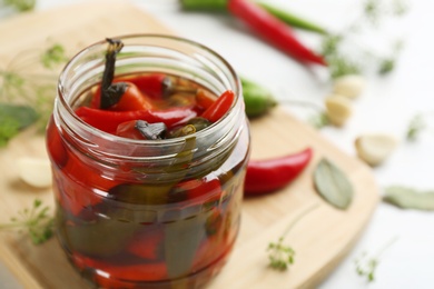 Photo of Glass jar of pickled chili peppers on table, closeup. Space for text