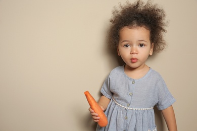 Photo of Cute African-American girl with carrot on color background. Space for text