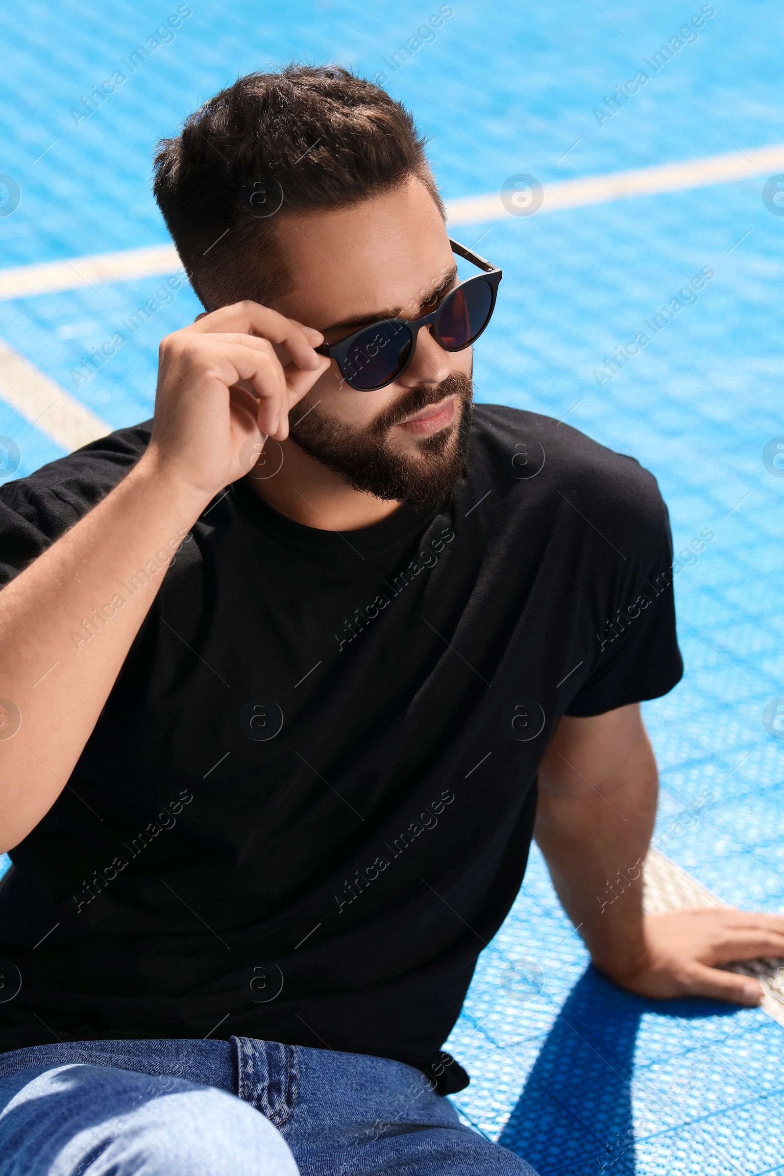 Photo of Handsome man in sunglasses on blue floor covering outdoors