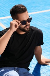 Handsome man in sunglasses on blue floor covering outdoors