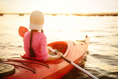 Photo of Little girl kayaking on river, back view. Summer camp activity