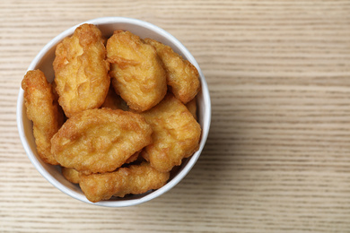 Bucket with tasty chicken nuggets on wooden table, top view. Space for text