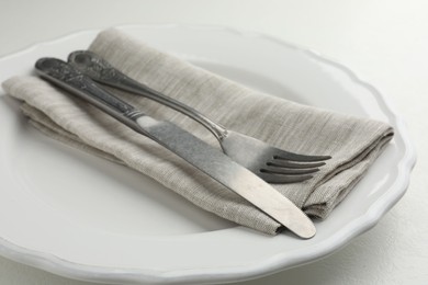 Stylish setting with cutlery, napkin and plate on white table, closeup