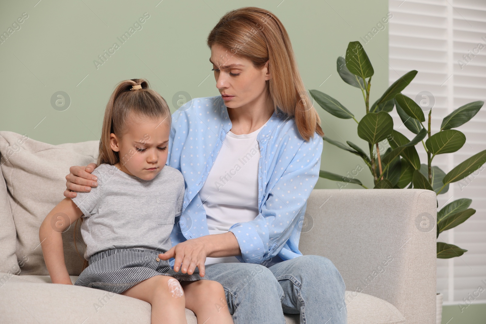 Photo of Mother applying ointment onto her daughter's knee on couch indoors