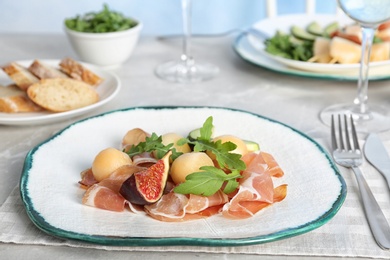 Plate with melon balls and prosciutto served on gray table