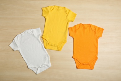 Photo of Different baby bodysuits on wooden background, top view