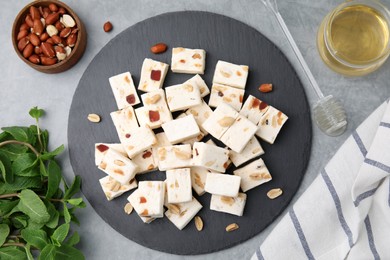 Photo of Pieces of delicious nutty nougat, peanuts, mint and honey on light gray table, flat lay