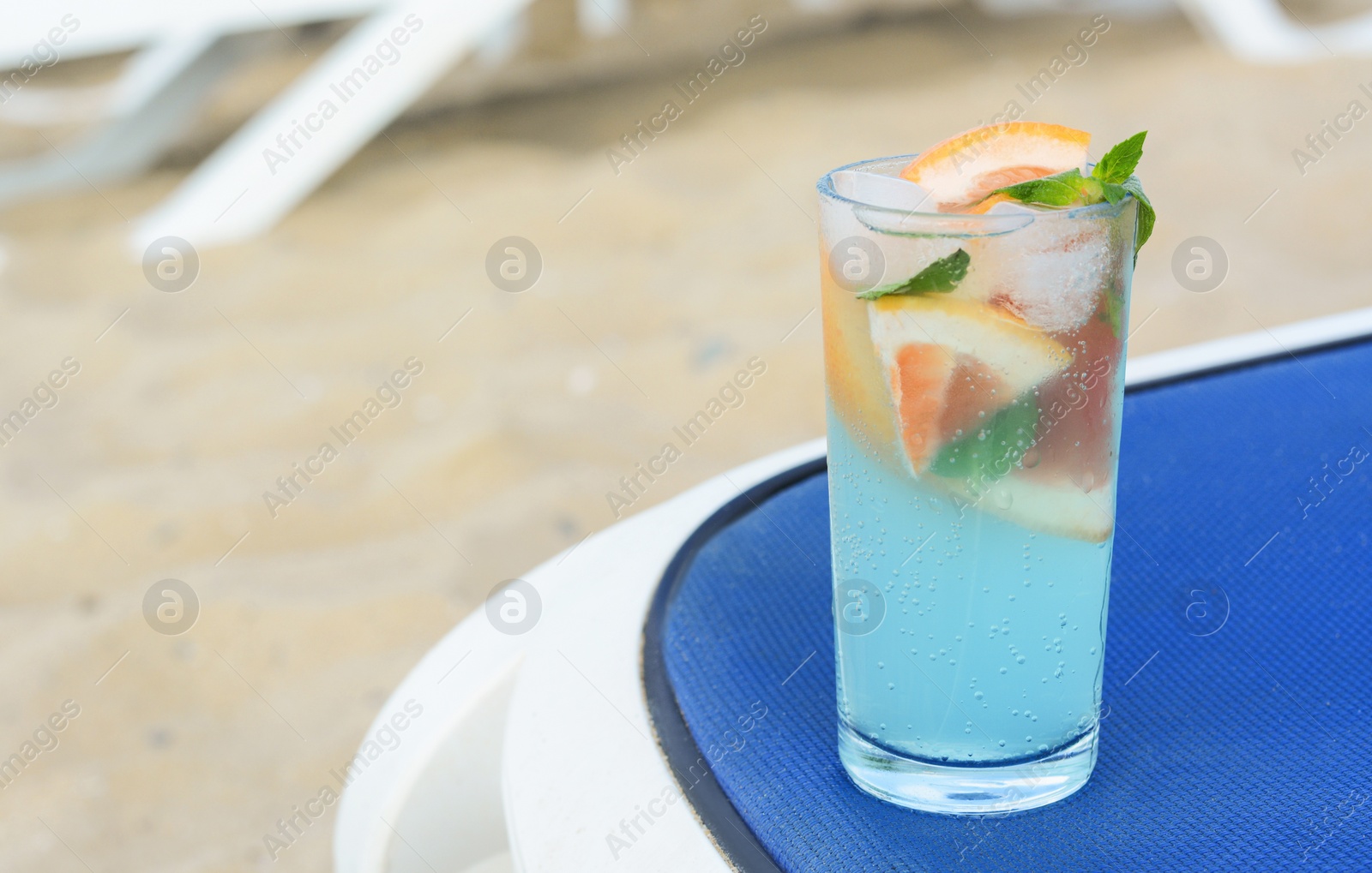 Photo of Glass of refreshing drink with grapefruit and mint on blue lounger at beach, space for text