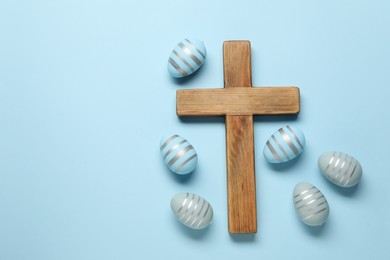 Photo of Wooden cross and painted Easter eggs on light blue background, flat lay. Space for text