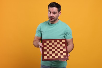 Photo of Adult man holding chessboard on orange background